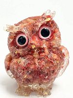 Front and slightly angled views of a resin owl figurine with embedded natural amethyst crystal shards. The owl has large black and pink eyes and a textured crystalline body.