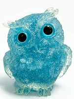 Front and slightly angled view of blue resin owl figurine embedded with natural amethyst crystal shards, showing large black eyes and detailed textured surface.