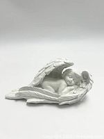 Front angled view of the white polyresin angel figurine showing the sleeping baby angel wrapped in large sculpted wings.