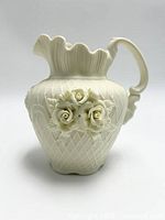 Front angle view of vintage ivory porcelain pitcher vase showing floral relief and handle