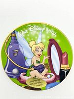 Front view of the mini ceramic plate showing Tinker Bell artwork with perfume bottle and lipstick design on a green background with Walt Disney World text.