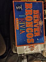 Photo showing the 1985 Denver Broncos Trivia Game box in blue and orange, with NFL logo and details: "For 2 or more players ages 8 to adult".
