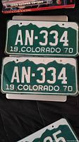 Two green and white 1970 Colorado license plates AN-334 stacked showing front side of plate with mountain design and embossed characters.