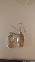 Pair of 925 sterling silver drop earrings with oval faceted citrine stones, shown lying flat with hook ear wires visible.
