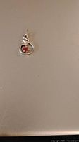 Front view of the 925 sterling silver pendant with a small round red ruby in a swirl design.