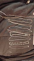 Photo showing nine assorted silver tone chains laid out on a dark cloth background. Chains are varied in style and thickness.