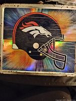 Close-up photo of the Denver Broncos metal lunch box showing helmet logo and edge wear.