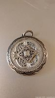 Photo showing front side of large silver Victorian locket with textured, engraved scrollwork and central diamond shape.
