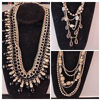 Multiple vintage gold tone necklaces displayed on black necklace stands showing bead, chain, and pendant designs.
