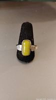 Front view of vintage handmade ring with rectangular yellow-green jade set in silver band on black ring display.