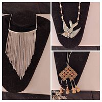 Photo of three vintage silver tone necklaces displayed on black necklace stands: fringe chain, bird pendant with beads, and geometric pendant with tassels.