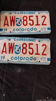 Pair of 1976 Colorado Centennial license plates with registration number AW 8512, displaying authentic 1976 registration decals and slight wear.