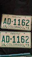 Two 1973 Colorado license plates with the number AD-1162 displayed on a dark surface.
