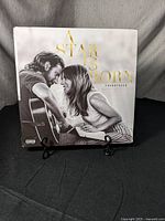 Front album cover featuring Lady Gaga and Bradley Cooper with guitar, title A Star is Born in gold lettering.