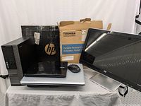 Overview of the entire computer lot showing HP tower, HP monitor, black mouse, and five laptops stacked with Toshiba box visible.