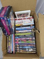 Box of assorted DVDs showing a mix of movie and TV show titles stacked vertically and horizontally inside a corrugated cardboard box.