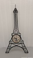 Front view of black metal Eiffel Tower shaped frame with central clock face showing time, clock and decorative details clearly visible.
