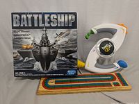 Photo of Battleship board game box, Bop-It game, and wooden Cribbage board showing painted track and pegs.