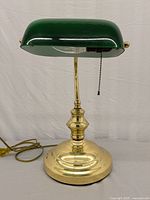 Front angled view of the lamp showing the brass base, stem, and green glass shade with pull chain switch and power cord.