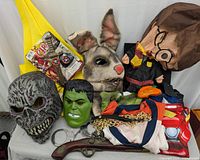 Photo of assorted Halloween masks, costumes, and decorations including a zombie mask, Hulk mask, rabbit head accessory, Harry Potter figure with mask, toy pistol, and handcuffs.