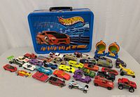 Full lot includes blue metal carrying tin with Hot Wheels cars arranged in front, various colors and styles, some vintage.