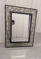 Front view of the decorative mirror showing the black inner frame and outer metal link frame in black and gold tones.