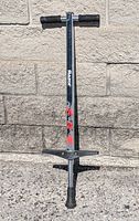 Front view of Razor pogo stick showing foam handles, vertical tube with logo, foot pegs, and rubber base tip against outdoor stone background.