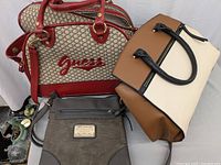 Photo showing red Guess purse with logo, two-tone tan and cream handbag, and gray crossbody bag with Dooney & Bourke plaque