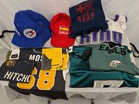 All items visible: jerseys, hats, towels, scarf spread in white bin