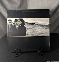 Front cover of U2 The Joshua Tree vinyl record album showing band members in a desert landscape with black and white photo.