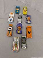 Top view of 11 vintage toy cars arranged on fabric surface, showing color variations and paint wear.