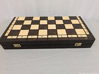 Closed view of wooden chess board with detailed alphanumeric notation and metal clasps on side for folding and storage.