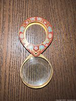 Magnifying glass showing the teardrop-shaped handle with floral cloisonné enamel decoration, gilded metal frame, and round lens.