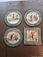 Four hand embroidered textiles displayed on wooden surface, three round with detailed embroidery of characters and one square with a different character, all bordered with ornate fabric trim.