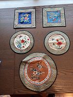 Set of five Chinese silk hand-stitched flower tapestries laid out on a wooden surface showing their overall design and sizes.