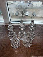 Three antique crystal cruet perfume bottles with intricately cut patterns and stoppers, placed on a wooden surface near a window with outdoor view.