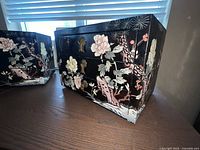 Photo showing front and side angle of vintage black lacquer chest with hand-painted crane birds and floral scene, including cast metal drawer handles.