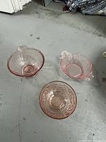 Three pink antique depression glass nut bowls placed on a concrete floor showing shape and color of each bowl.