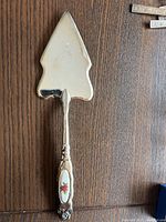 Full view of the silver pie cutter showing the spear-shaped blade and the handle with the floral inlay.