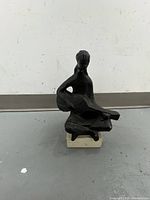 Front view of black abstract seated figure sculpture with guitar on white marble base