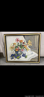 Full view of framed abstract still life painting with flowers in a vase on white cloth.