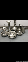 Front view of seven silverware items including vases, pitchers, bowls, and a salt shaker.