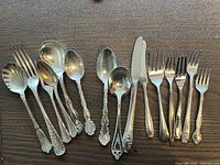 Photo showing 14 pieces of various silverware including forks, spoons, butter knife, and serving spoon arranged on wooden surface.