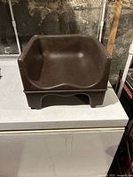 Front view of brown plastic child booster seat showing seat contour and raised backrest.
