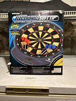 Front box image of Sportcraft CX2500 electronic soft tip dartboard showing dartboard with red and blue darts, digital scoreboard, and feature highlights on box.