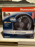 Front view of the Honeywell Power Air Circulator fan box highlighting key features such as 30% quieter operation, 90 degree fan head pivot, and carry handle.