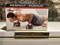 Photo showing the original boxed Perfect Pushup rotating pushup handles product. The box highlights features such as unique rotating handles, steel handle with soft rubber grips, and includes instructional DVD.