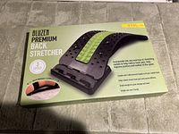 Photo of the boxed premium back stretcher showing the product and its 3 adjustment levels on carpeted surface.