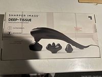 Box showing the Sharper Image Deep-Tissue Percussion Massager with images of 3 attachments and ergonomic handle on packaging.