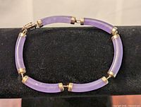 Bracelet laid flat on black surface showing full curved jade and gold design